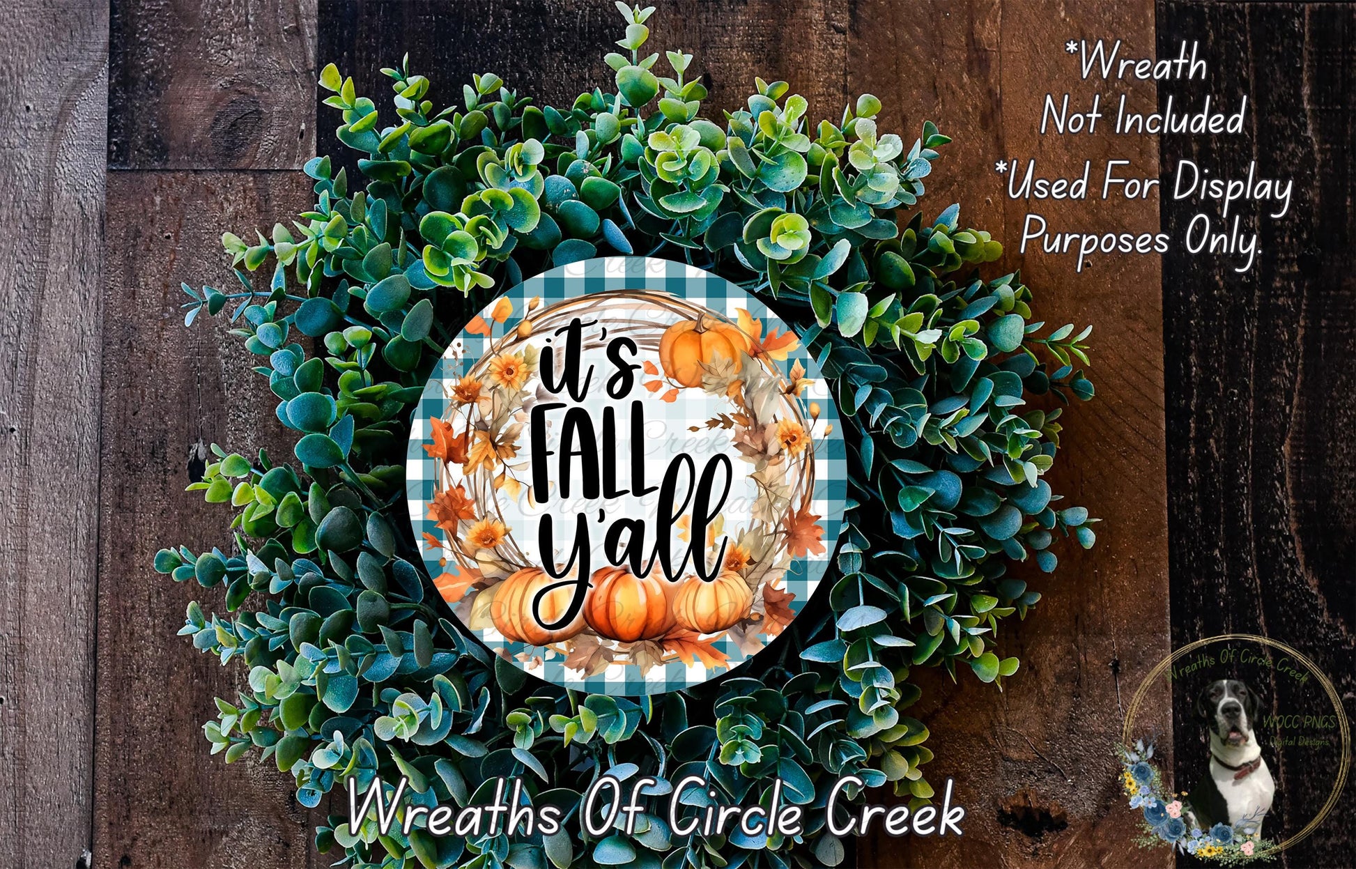a wreath made of various green and orange leaves, with a central circular design that says "It's Fall Yall". The wreath is displayed on a wooden surface, and there is a small dog in the bottom right corner of the image.