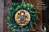 a wreath with a scarecrow and sunflowers, surrounded by greenery. The wreath is displayed on a wooden surface, and there is a small dog in the bottom right corner.