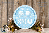 a blue circular sign with the text "Dashing through the SNOW" written on it, surrounded by a wreath of flowers and a wooden background.