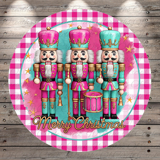 A circular design featuring three nutcracker characters in pink and teal outfits, standing in a row and holding a drum. The text "Merry Christmas" is displayed below the nutcracker characters.