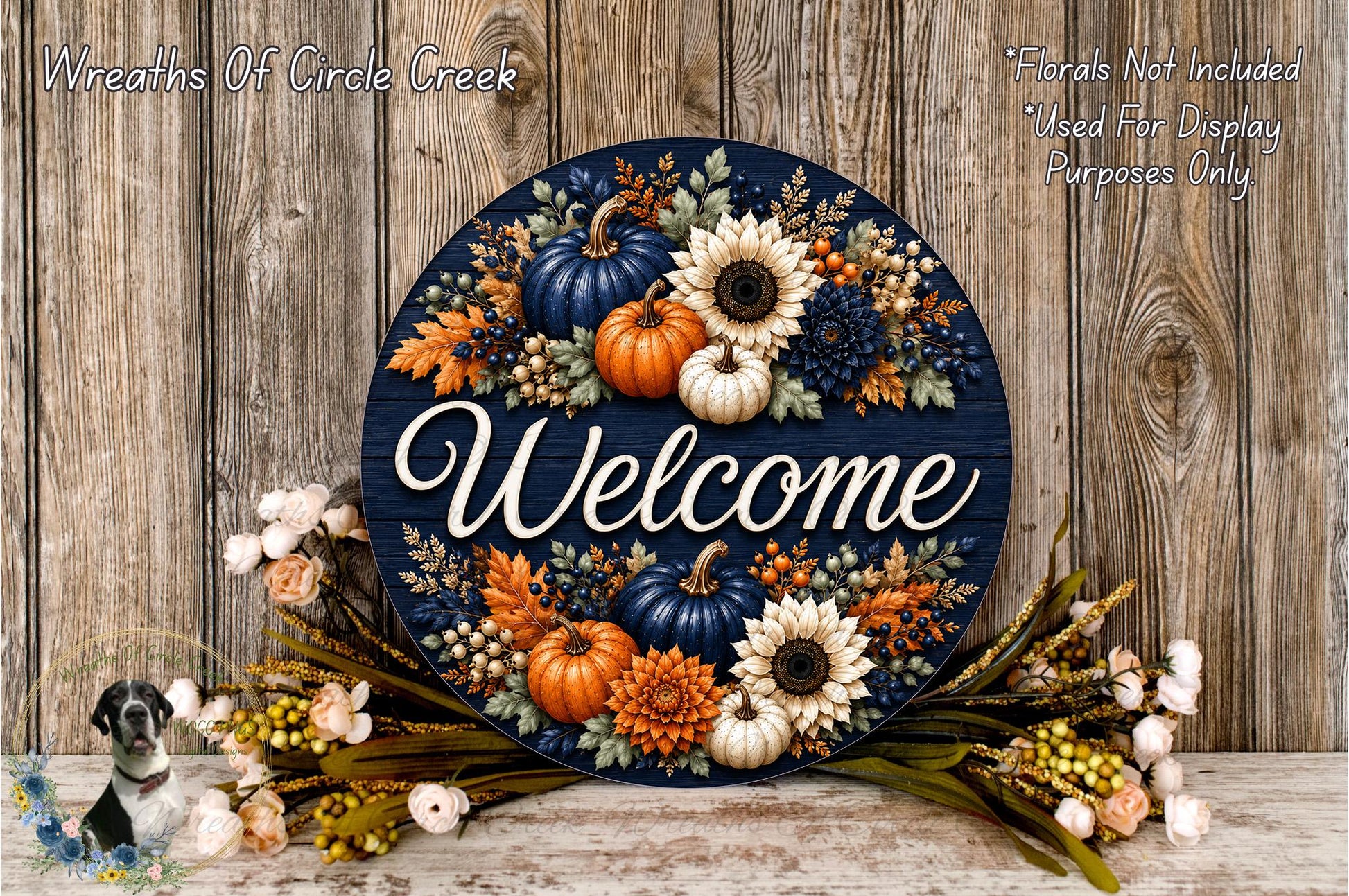 a decorative welcome sign with a floral design, surrounded by autumn-themed flowers and foliage. The sign is placed on a wooden surface, and there is a small bird figurine in the bottom left corner.