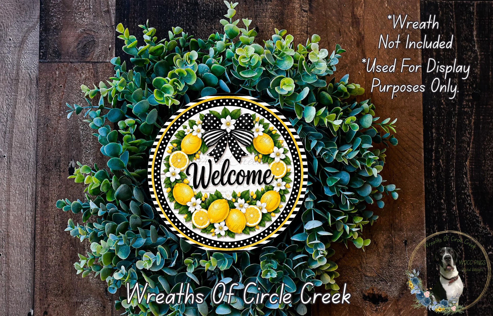 A wreath made of green leaves and yellow flowers, with a white and black bow, and the word "Welcome" written on it. The wreath is displayed on a wooden surface.