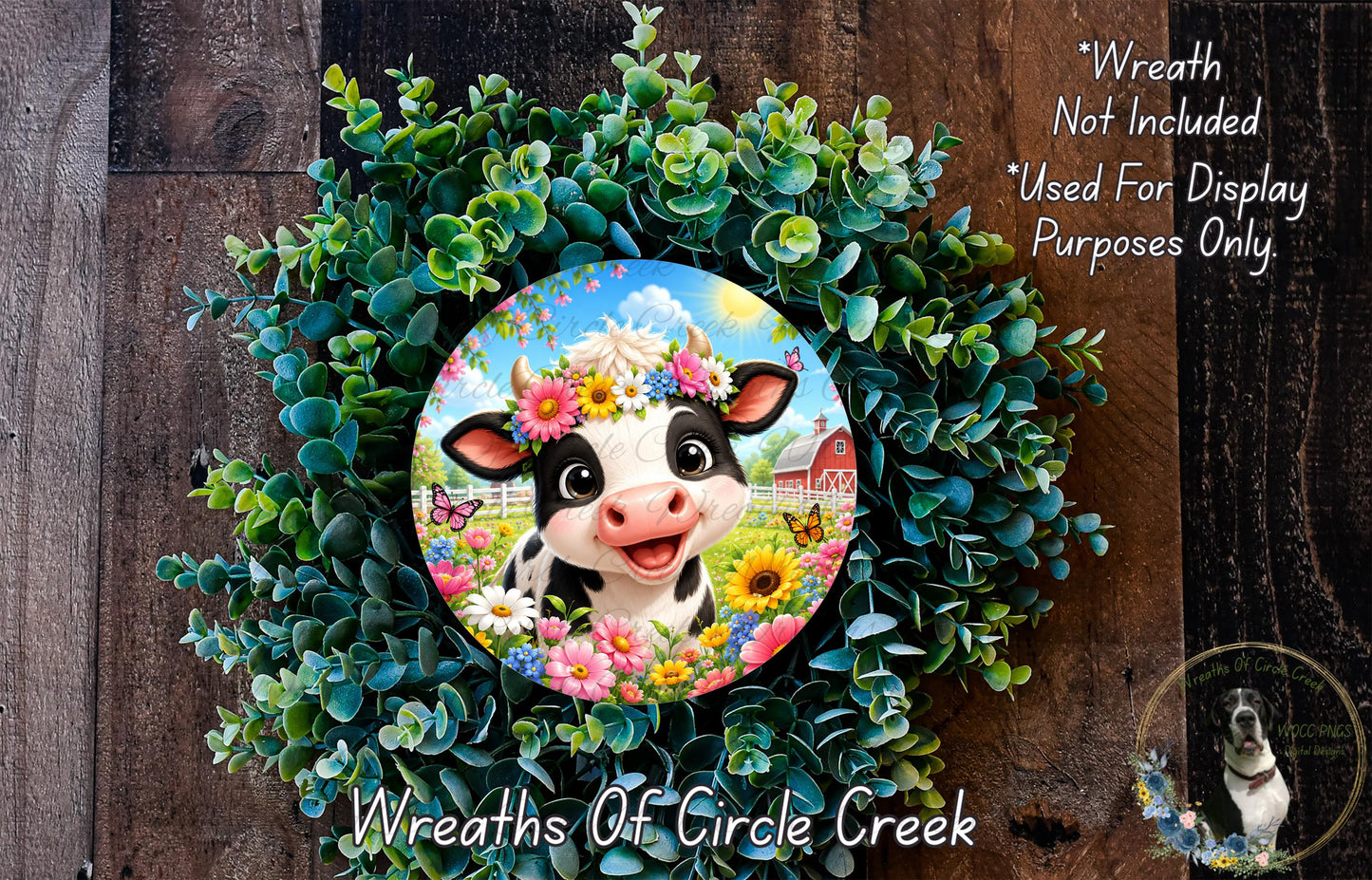 a wreath with a cow wearing a flower crown, surrounded by a lush green wreath. The cow is smiling and appears to be the focal point of the wreath. The wreath is set against a wooden background, and there is a small dog visible in the bottom right corner of the image.
