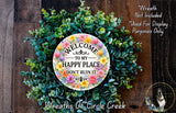 a wreath made of various green plants and flowers, with a circular sign in the center that reads "Welcome to my happy place don't ruin it".