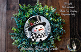 A wreath featuring a snowman made of green leaves and a black top hat, with a red bow on the snowman's face.