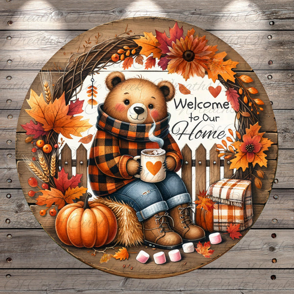 A round wooden sign with a teddy bear sitting on a bench, holding a mug and surrounded by autumn decorations such as leaves, flowers, and a pumpkin.