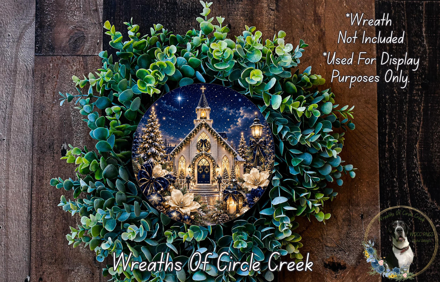 A wreath with a picture of a church and Christmas trees, surrounded by greenery, hangs on a wooden wall.