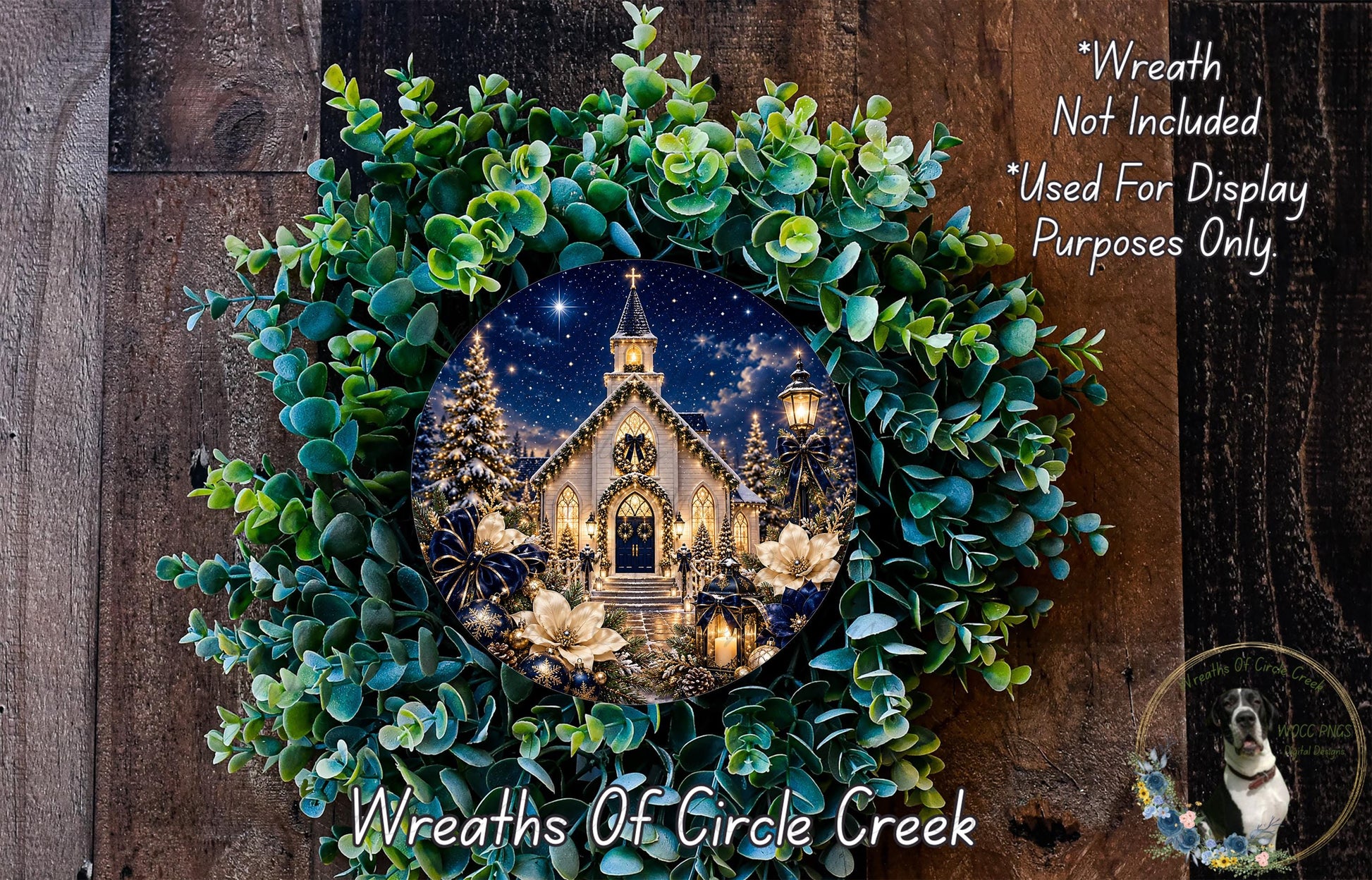 A wreath with a picture of a church and Christmas trees, surrounded by greenery, hangs on a wooden wall.