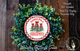 A wreath made of evergreen branches and a circular sign with text, placed on a wooden surface.