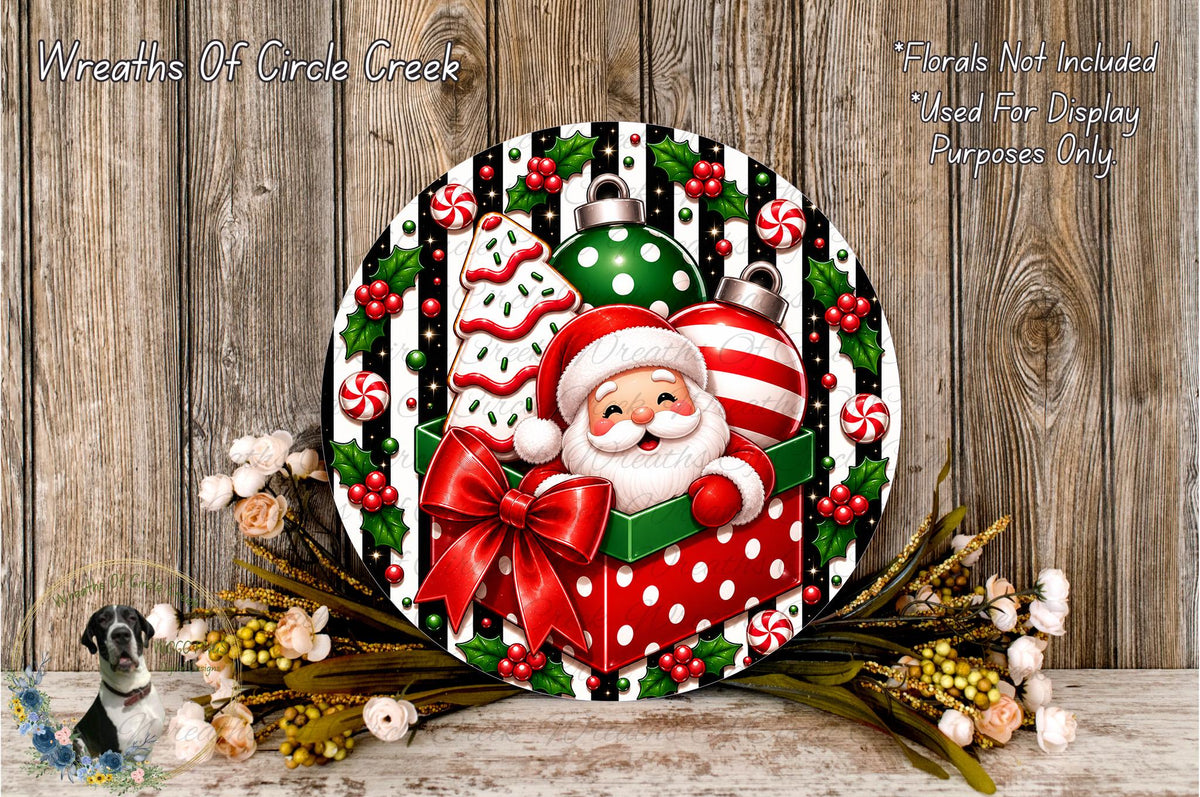 A festive Christmas wreath featuring a smiling Santa Claus in a gift box, surrounded by holiday decorations such as ornaments, tinsel, and flowers.