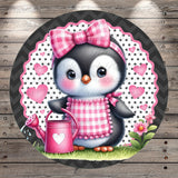 A cute cartoon penguin wearing a pink bow and apron, holding a pink watering can, surrounded by hearts and flowers on a wooden background.