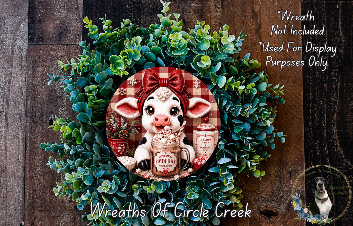 a wreath with a cow figurine in it, surrounded by greenery. The cow is wearing a red bow and is holding a mug with a red and white label. The wreath is displayed on a wooden surface, and there is a text overlay that reads "Wreath Not Included * Used For Display Purposes Only".