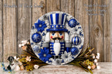 A decorative nutcracker wreath with blue and silver ornaments, surrounded by flowers and pine cones, placed on a wooden surface.