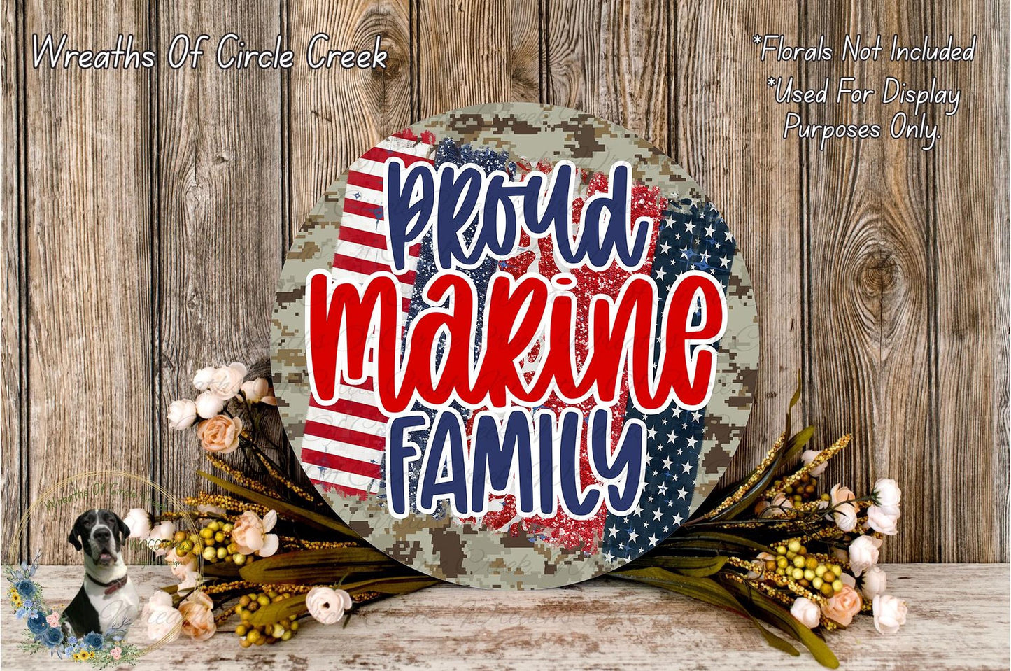a patriotic-themed wreath with the text "Proud Marine Family" displayed prominently. The wreath is surrounded by a floral arrangement and is set against a rustic wooden background.