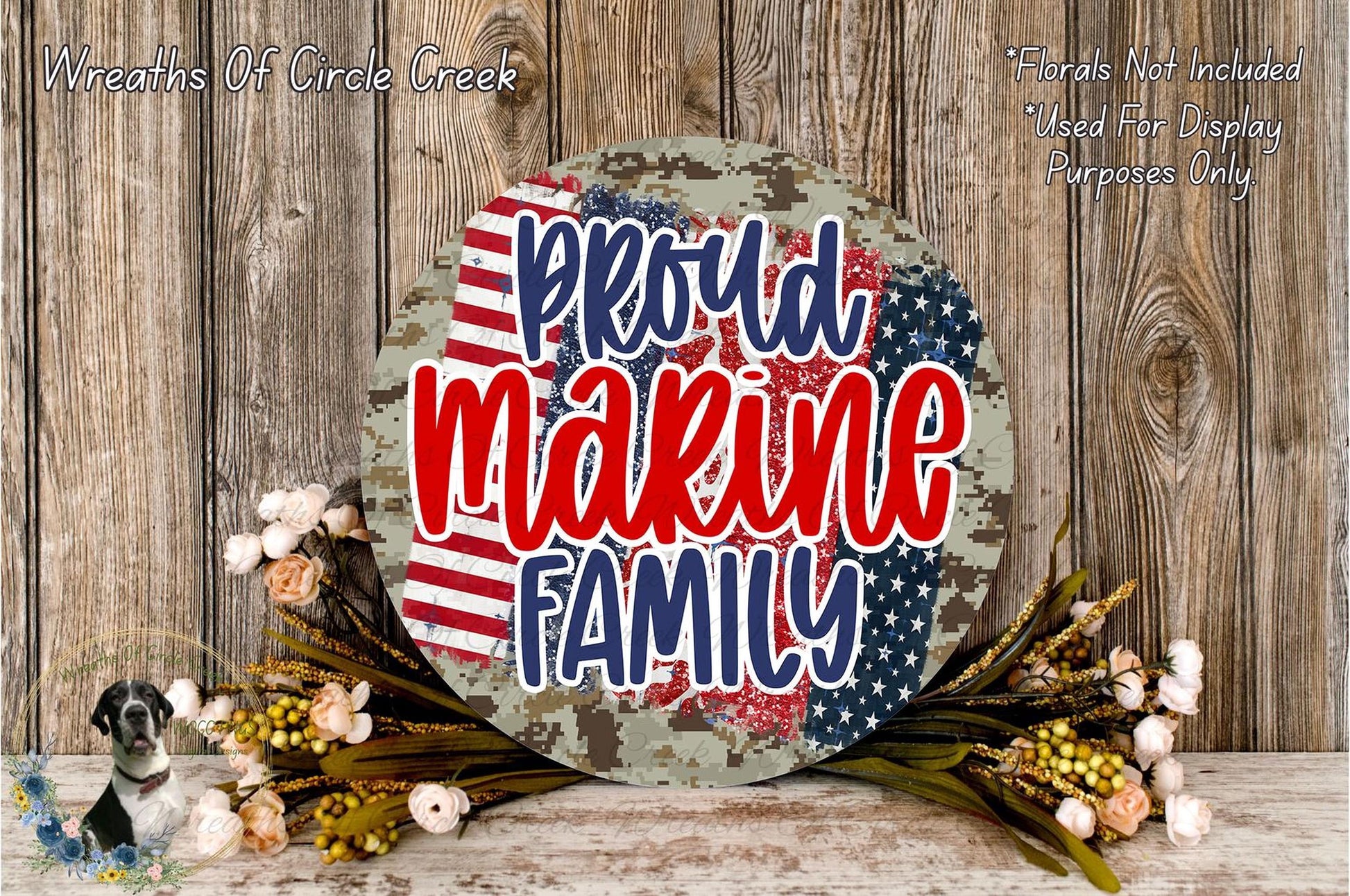 a patriotic-themed wreath with the text "Proud Marine Family" displayed prominently. The wreath is surrounded by a floral arrangement and is set against a rustic wooden background.