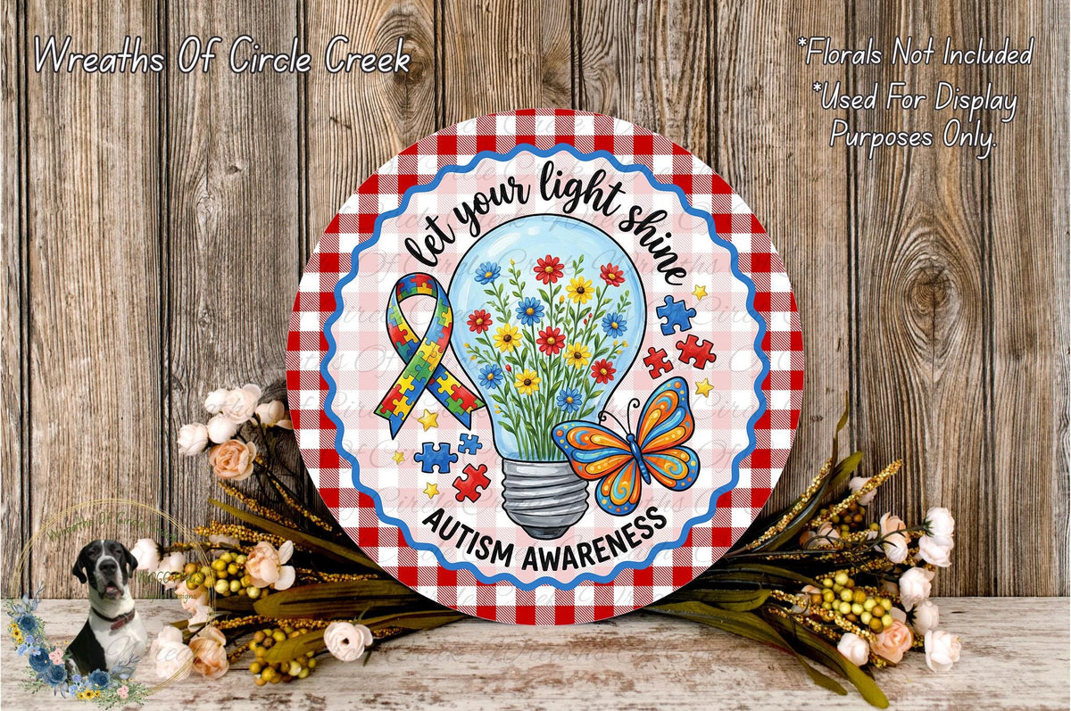 a round sign with a floral design and a light bulb inside, surrounded by flowers and a butterfly. The sign has the text "Let your light shine" and "Autism Awareness" written on it.