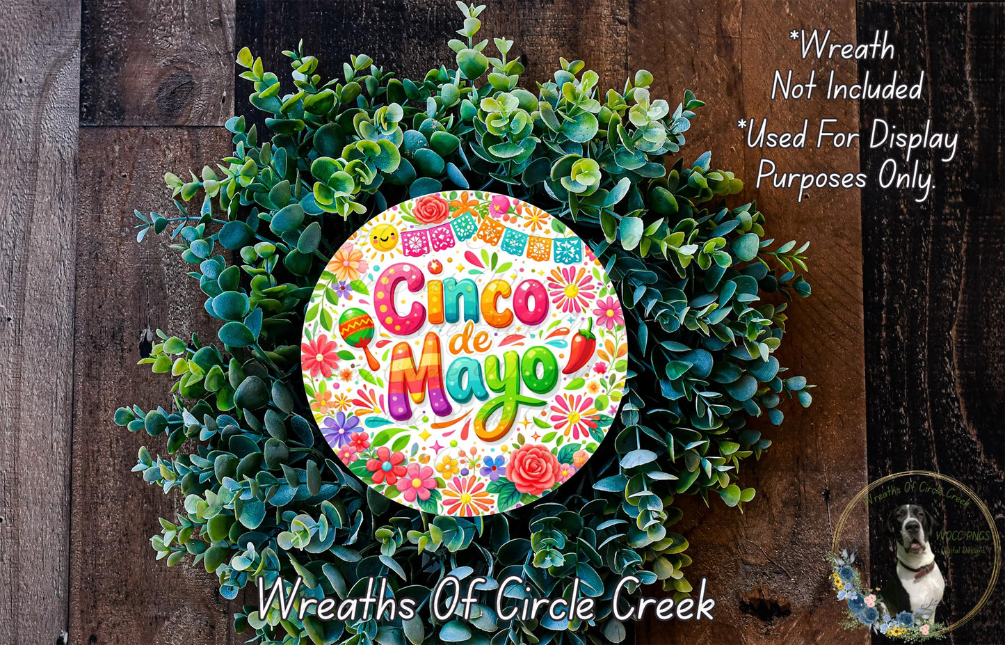 A colorful wreath made of green leaves and flowers, with a circular sign that says "Cinco de Mayo" in the center.