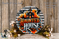 a Halloween-themed sign with a house and bats, surrounded by flowers and placed on a wooden surface.