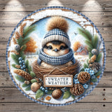 A small bird wearing a blue and white hat and scarf sits in a nest surrounded by pine cones, pine needles, and other winter-themed decorations. The bird is wearing a sign that says " sweater weather".