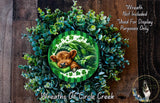 a wreath with a brown cow resting on it, surrounded by green foliage. The wreath is displayed on a wooden surface, and there is a small dog visible in the bottom right corner of the image.