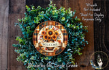 a wreath made of various green plants and flowers, with a decorative plate in the center displaying the word "WELCOME".