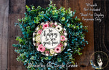 A wreath made of various green and pink flowers, with a sign that says "So happy to see your face" in the center.