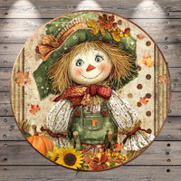 A round, decorative plate featuring a cheerful scarecrow with a hat, scarf, and overalls, surrounded by autumn leaves, flowers, and a pumpkin.