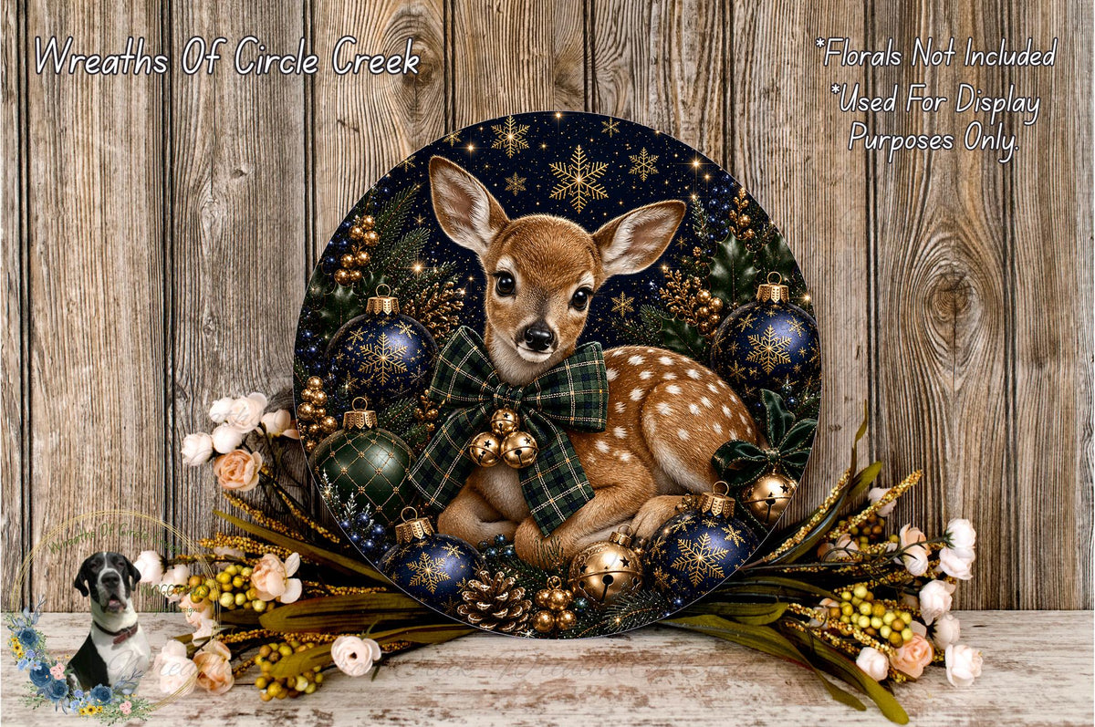 A decorative wreath featuring a deer surrounded by various holiday ornaments, including blue and gold balls, pine cones, and flowers, set against a wooden background.