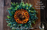 A wreath made of various autumn-themed elements, including a turkey, sunflowers, pumpkins, and greenery, is displayed on a wooden surface.