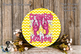 a decorative round sign with the text "Crawfish season" and a colorful design of pink and yellow lobsters against a yellow and white chevron pattern. The sign is surrounded by a floral arrangement and placed on a wooden surface.