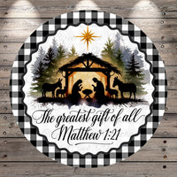 A circular design featuring silhouettes of a nativity scene with a man, woman, baby, and animals in a manger, surrounded by a forest and a star. The text "The greatest gift of all Matthew 1:21" is displayed below the nativity scene.