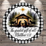 A circular design featuring silhouettes of a nativity scene with a man, woman, baby, and animals in a manger, surrounded by a forest and a star. The text "The greatest gift of all Matthew 1:21" is displayed below the nativity scene.