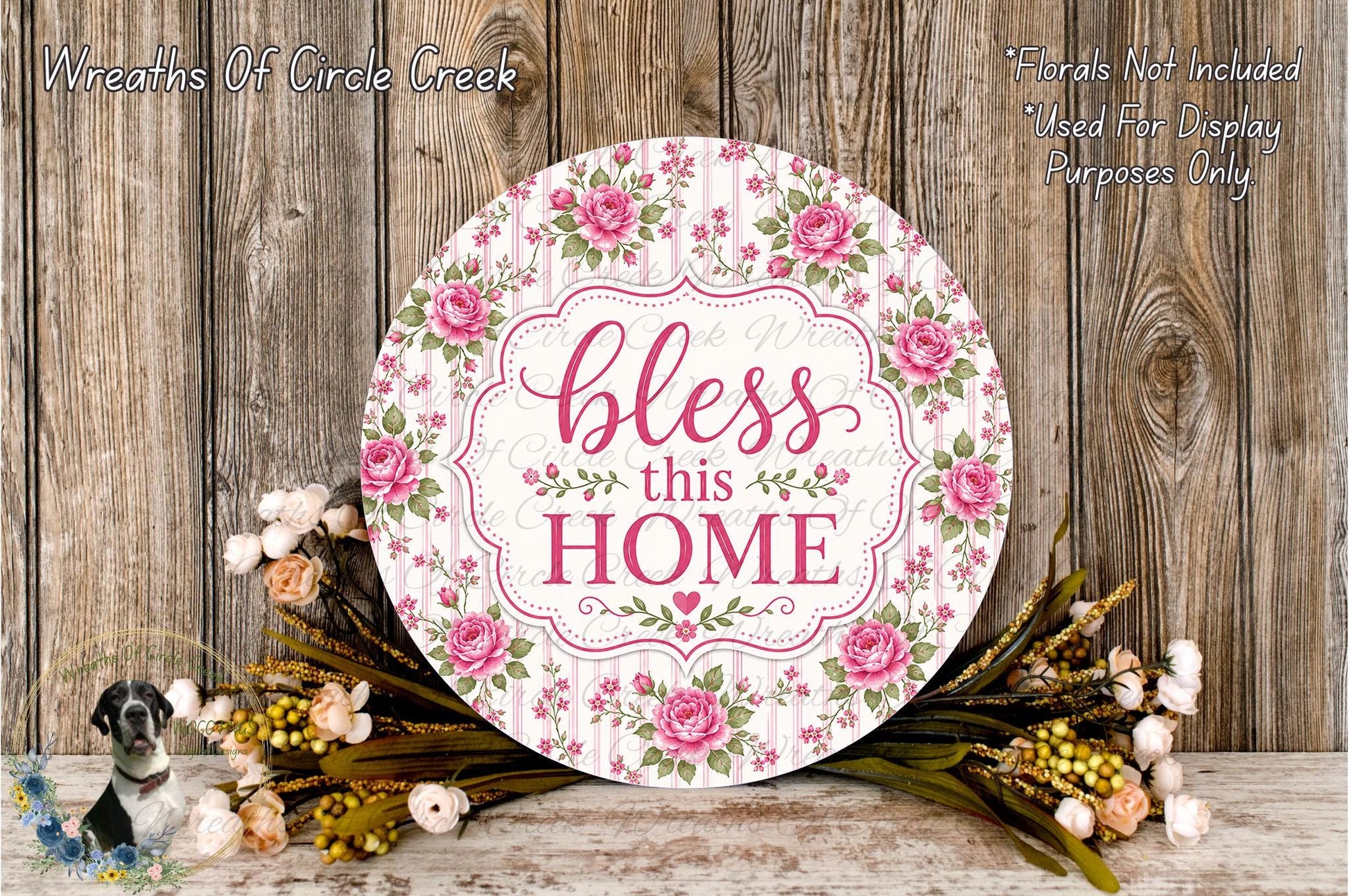 a round sign with a floral design and the text "bless this home" displayed on it, surrounded by a bouquet of flowers and a wooden background.