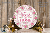 a round sign with a floral design and the text "bless this home" displayed on it, surrounded by a bouquet of flowers and a wooden background.