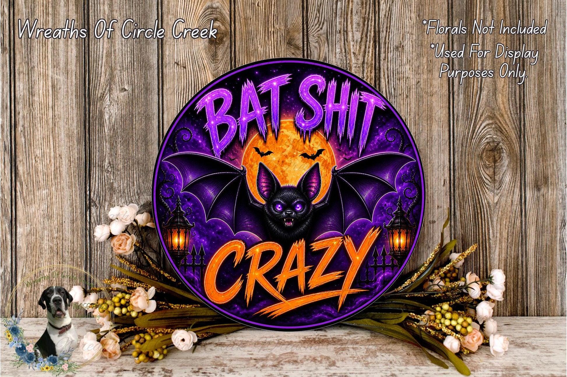 a Halloween-themed sign with a bat and the text "Bat Shit Crazy" in a purple and orange color scheme. The sign is surrounded by flowers and placed on a wooden surface.
