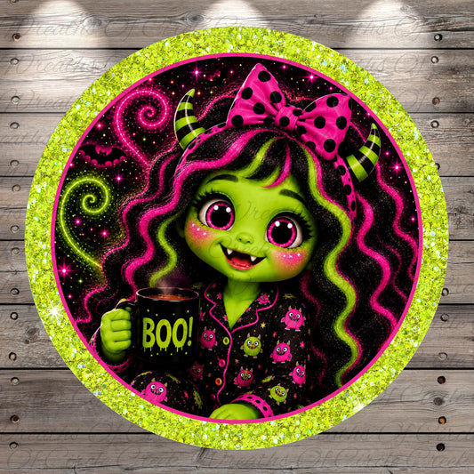 A green-skinned, horned girl with large eyes and a bow in her hair is holding a mug with the word "BOO!" written on it, surrounded by a glittery, circular frame with a green border.