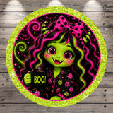 A green-skinned, horned girl with large eyes and a bow in her hair is holding a mug with the word "BOO!" written on it, surrounded by a glittery, circular frame with a green border.