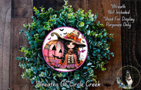 a Halloween-themed wreath with a pumpkin and a girl wearing a witch's hat. The wreath is surrounded by green foliage and has a "Happy Halloween" message.