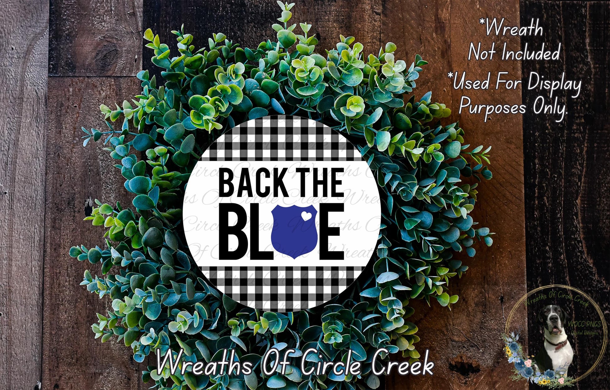 a wreath made of green leaves and a blue shield with the text "BACK THE BLUE" displayed on it. The wreath is placed on a wooden surface, and there is a small dog in the bottom right corner of the image.