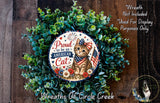 A wreath made of green leaves and flowers, with a circular sign featuring a cat and an American flag, placed on a wooden surface.