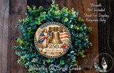 a wreath with a patriotic design, including a bell and an American flag, surrounded by greenery. The wreath is labeled as "250 Years of Liberty" and is displayed on a wooden surface.