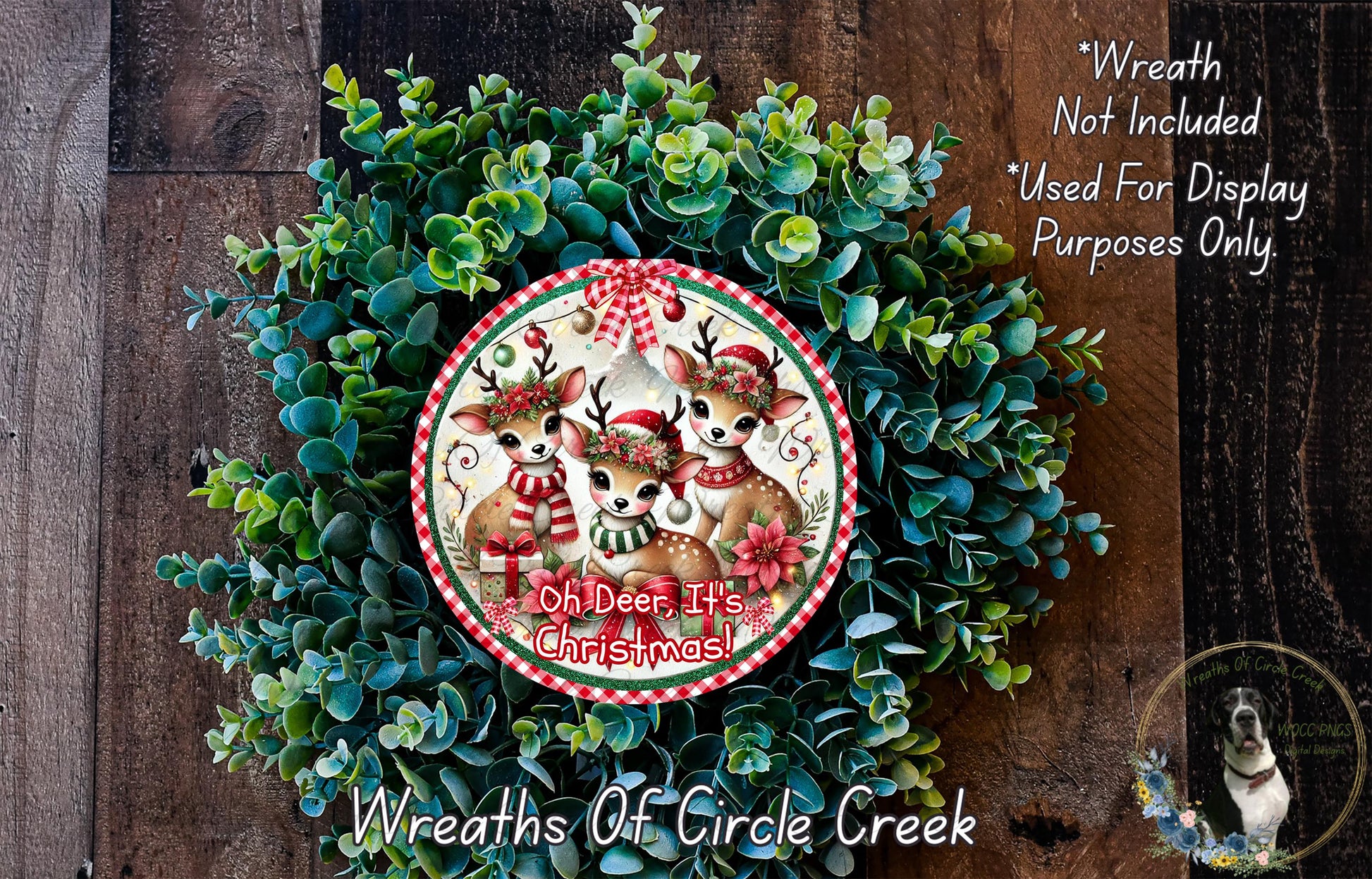A Christmas wreath made of green foliage and featuring three deer wearing Santa hats. The deer are wearing red and white scarves and have antlers. The wreath is displayed on a wooden surface.