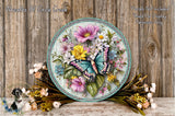A decorative round wreath with a butterfly and various colorful flowers, placed on a wooden surface.