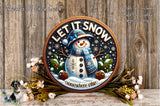 A decorative snowman sign with the text "LET IT SNOW somewhere else" surrounded by pine cones, pine branches, and flowers, placed on a wooden surface.