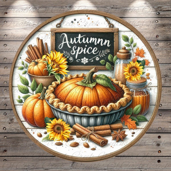 The image is a decorative arrangement featuring a pumpkin pie surrounded by autumn-themed elements such as sunflowers, cinnamon sticks, and a chalkboard sign that reads "Autumn spice".
