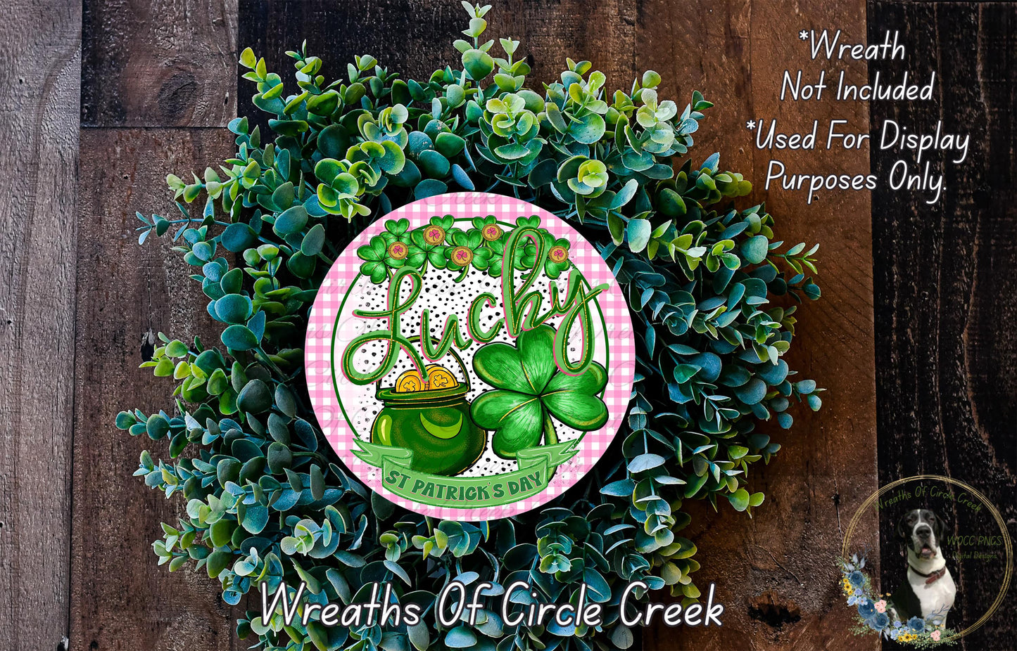 A wreath made of green leaves and a clover, with a pink and white circular sign featuring the word "Lucky" and an illustration of a pot of gold.