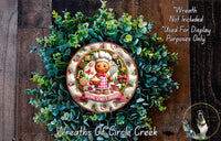 A wreath made of green foliage and featuring a gingerbread man figure, with a decorative plate in the center displaying the text &quot;Baking Spirits Right&quot;.