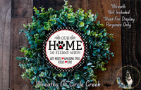 A wreath made of green leaves and a circular sign with the text "OUR HOME is filled with WET Noses WAGING Tails KISSES LOVE" is displayed on a wooden surface.