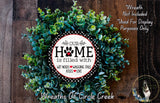 A wreath made of green leaves and a circular sign with the text "OUR HOME is filled with WET Noses WAGING Tails KISSES LOVE" is displayed on a wooden surface.