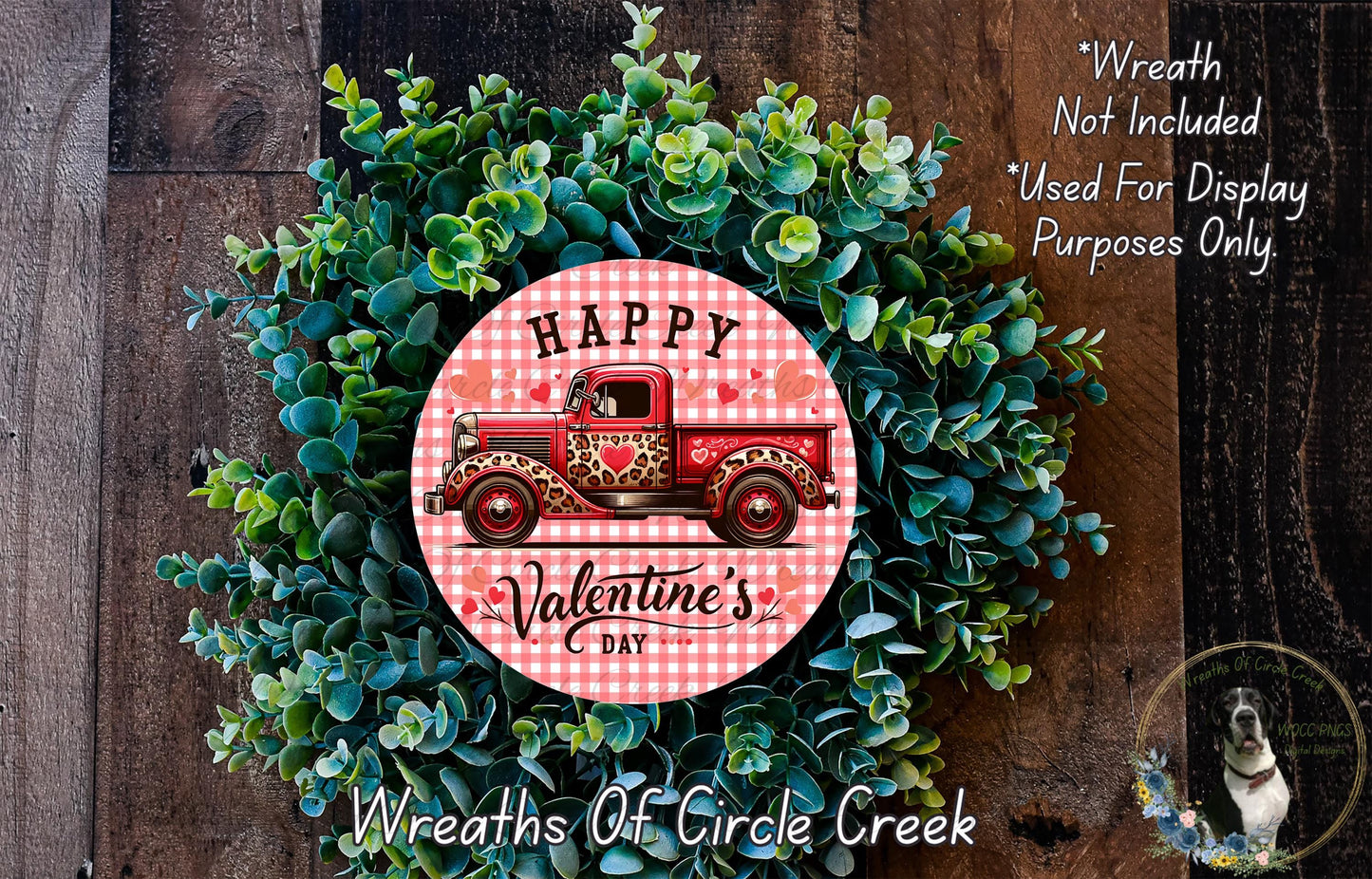 a wreath made of green foliage and a red truck with a "Happy Valentine's Day" sign on it. The wreath is displayed on a wooden surface, and there is a small dog in the bottom right corner of the image.